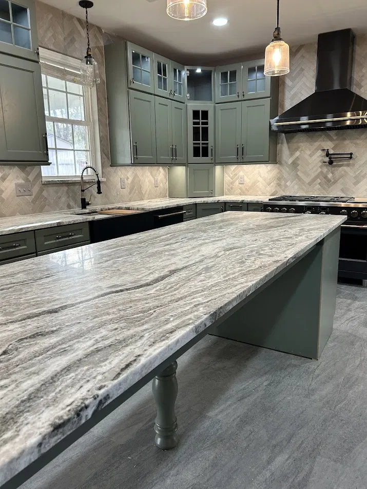 Kitchen remodel with sage green cabinets, massive marble island, and herringbone tile backsplash by CNB Renovations